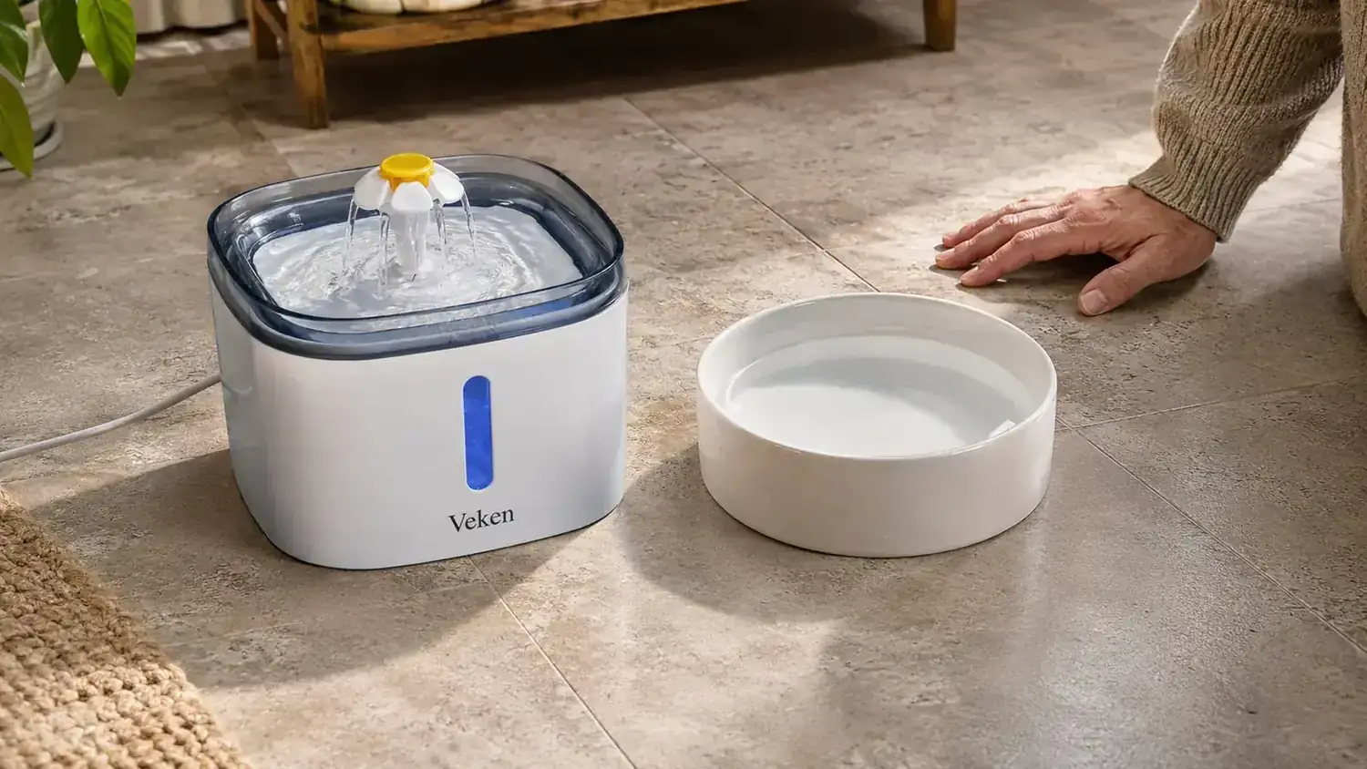 Side-by-side view of a ceramic water bowl and a Veken pet fountain placed on a tile floor